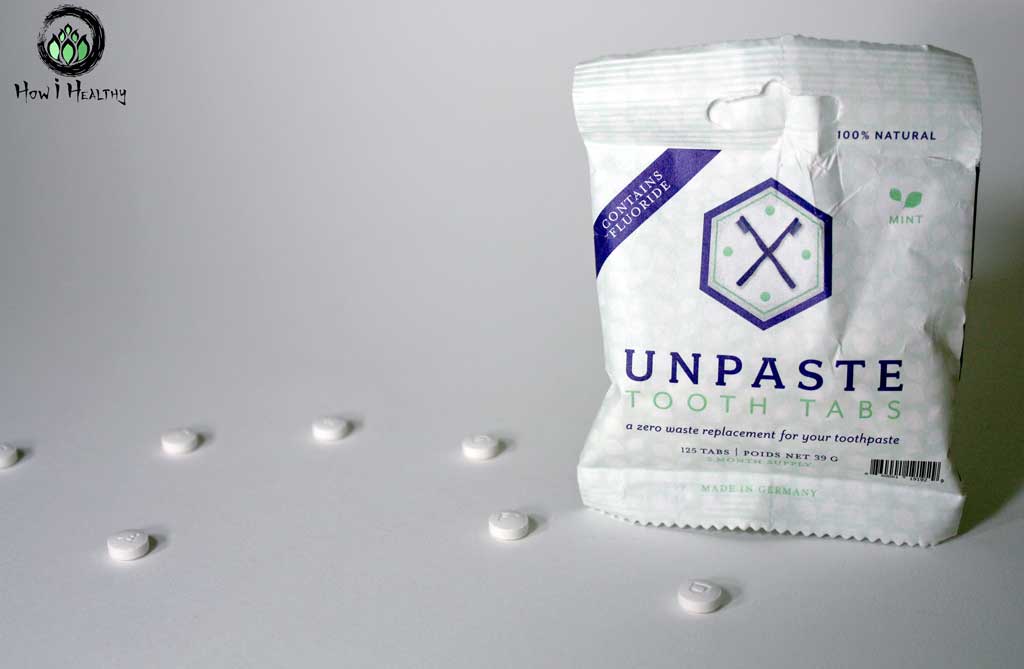 Seven water-free tooth tablets on white table beside Unpaste bag.