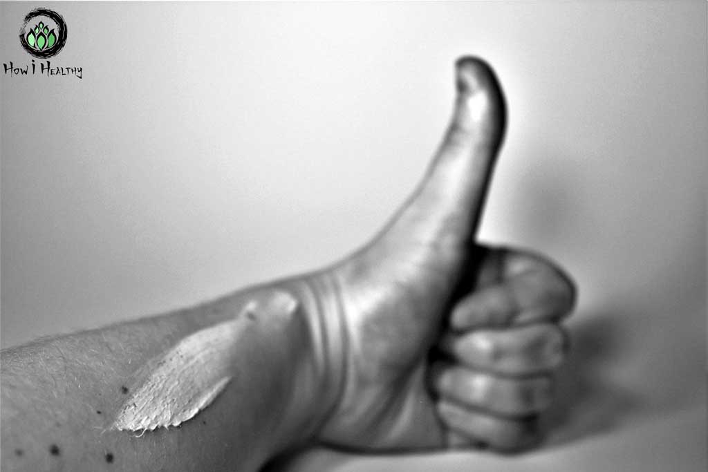 Smear of sunscreen on freckled forearm with a thumbs up hand gesture.